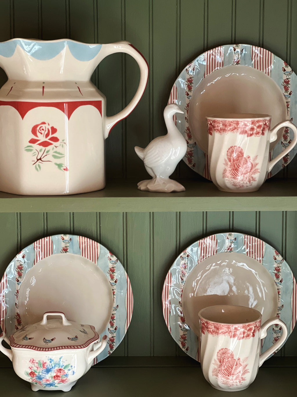 Vintage-style ceramic tableware with floral patterns on a green wooden shelf.