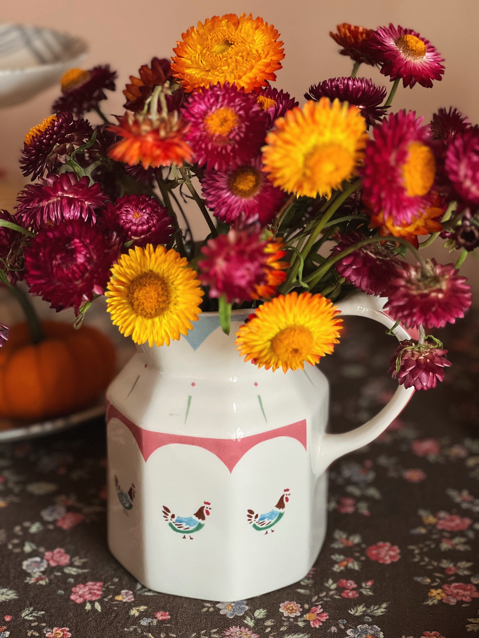 Colorful flowers in a white pitcher with fox design on a floral tablecloth.