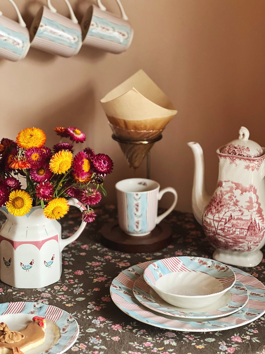 Tea set with teapot, cups, and plates on a floral tablecloth.