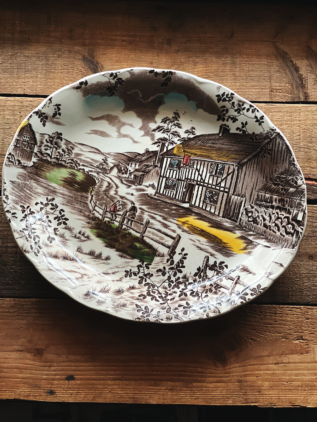 Decorative plate with a rustic scene of a cabin on a wooden surface