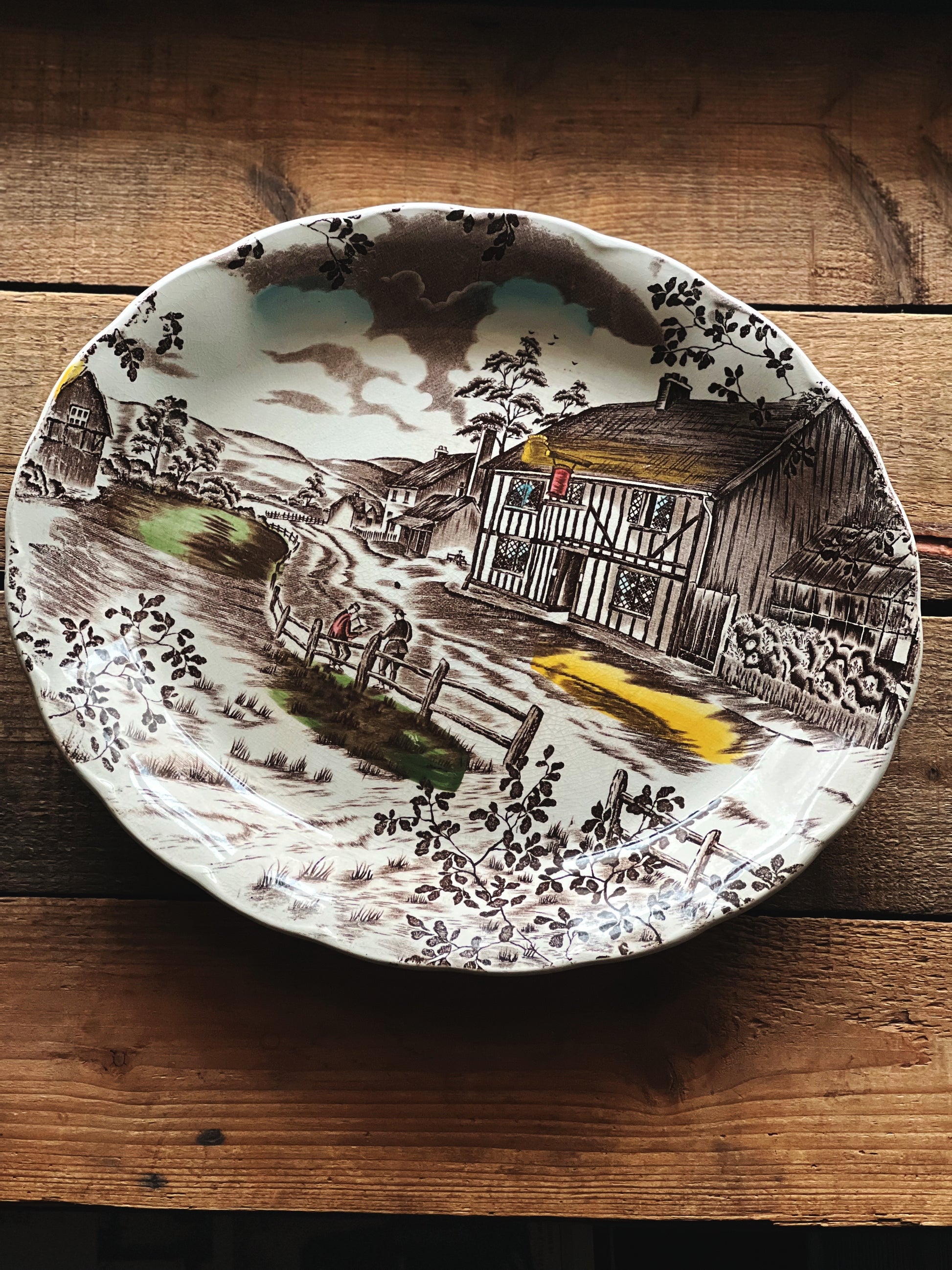 Decorative plate with a rustic scene of a cabin on a wooden surface