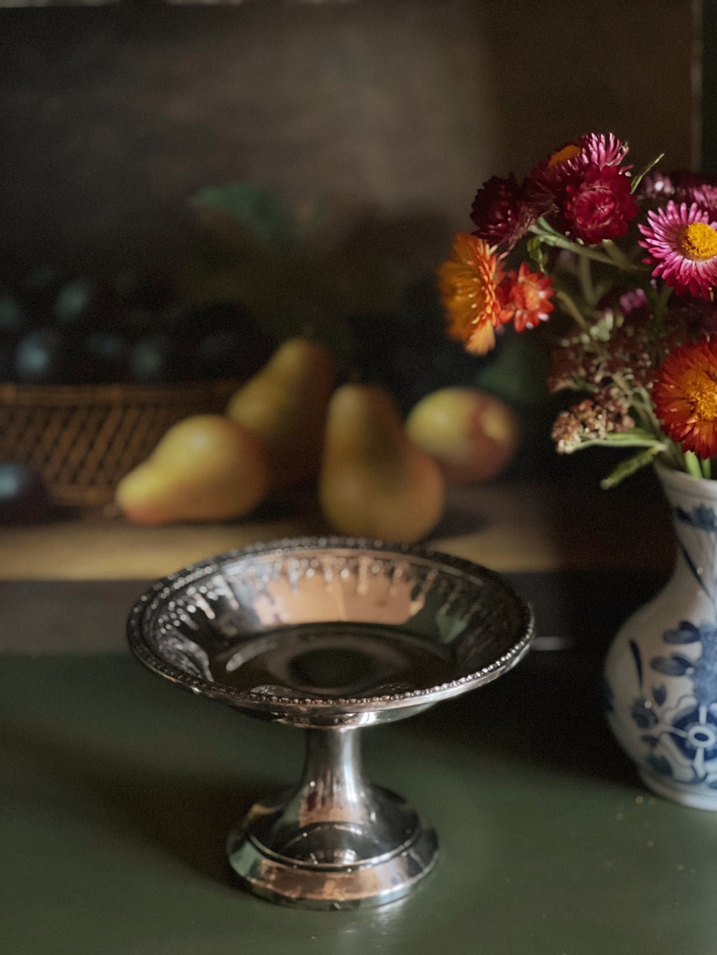 Silver dish on a table with pears and a vase of flowers in the background