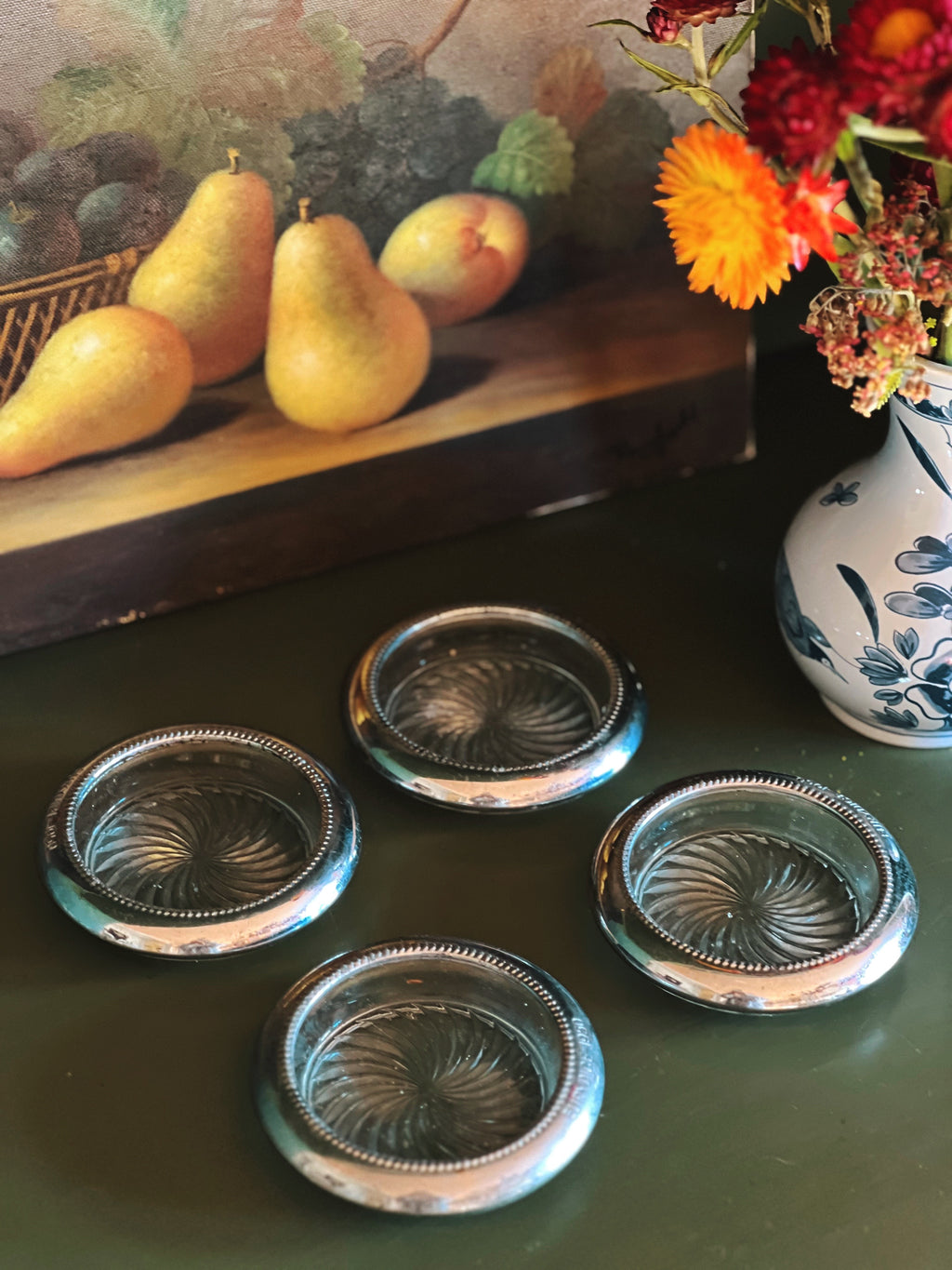 Set of four decorative glass coasters on a green surface with pears and flowers in the background.