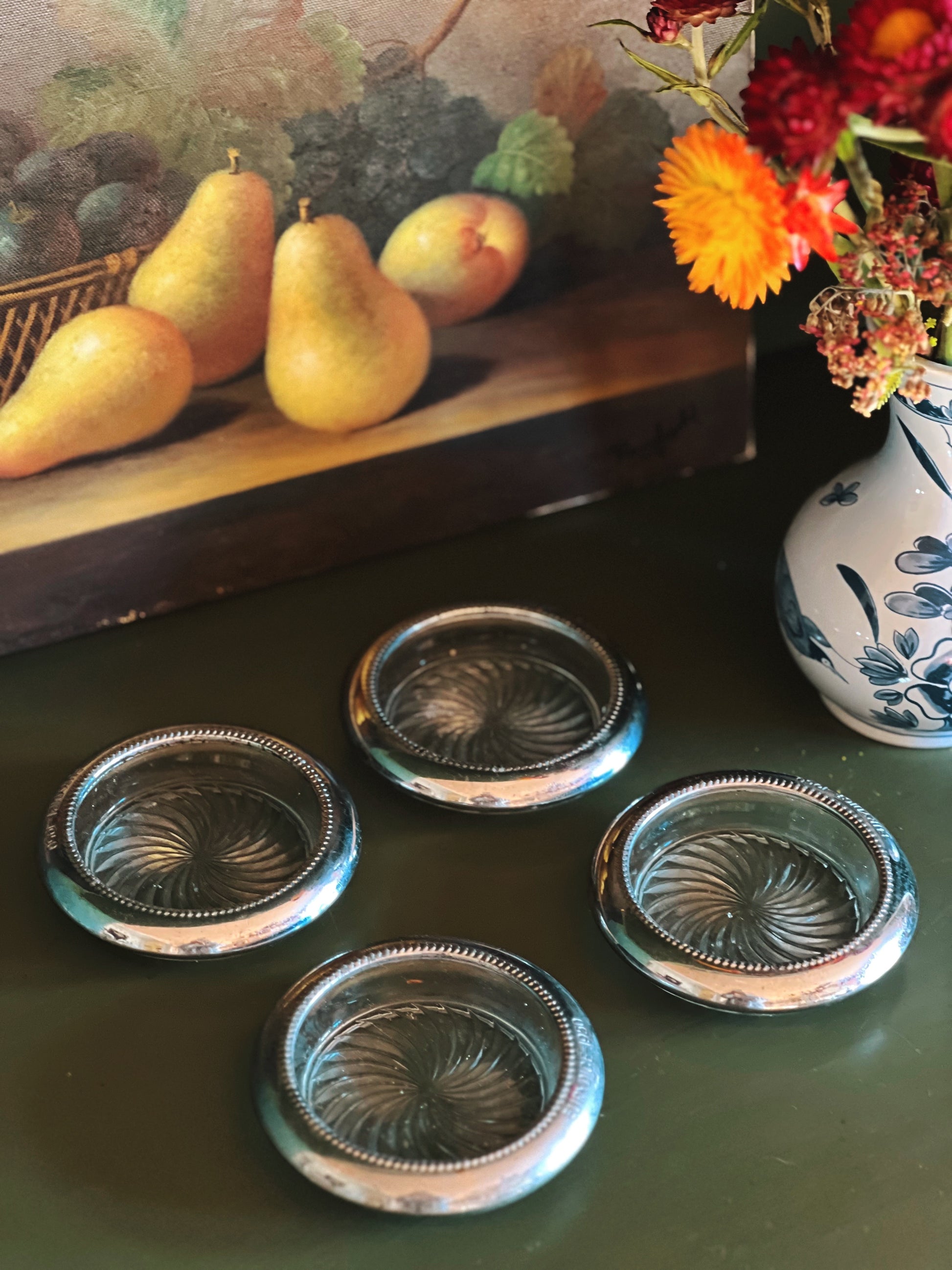 Set of four decorative glass coasters on a green surface with pears and flowers in the background.