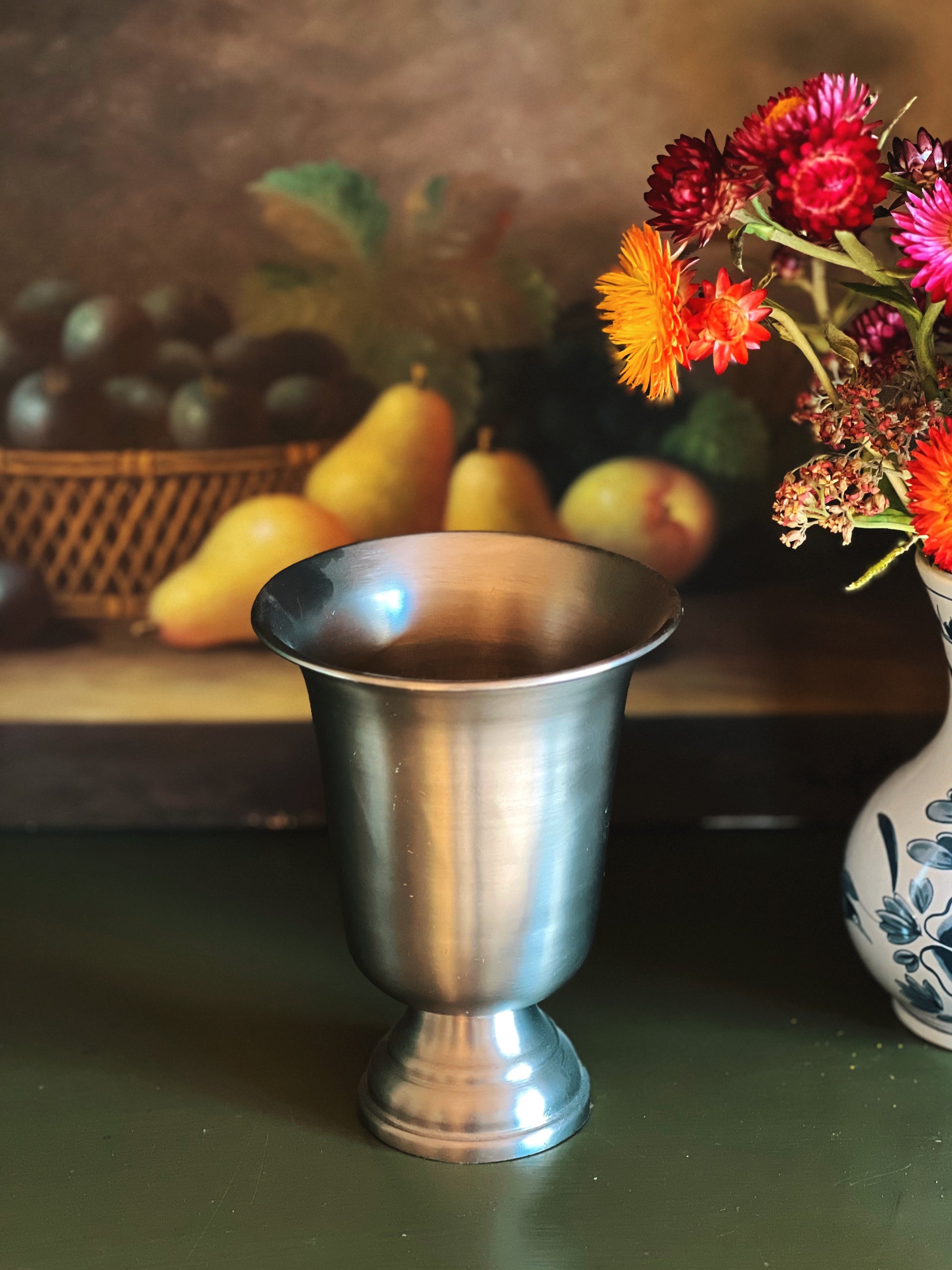 Silver goblet on a table with fruits and flowers in the background