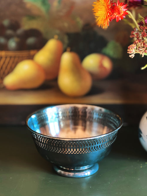Silver bowl with intricate design on a table with pears and flowers in the background