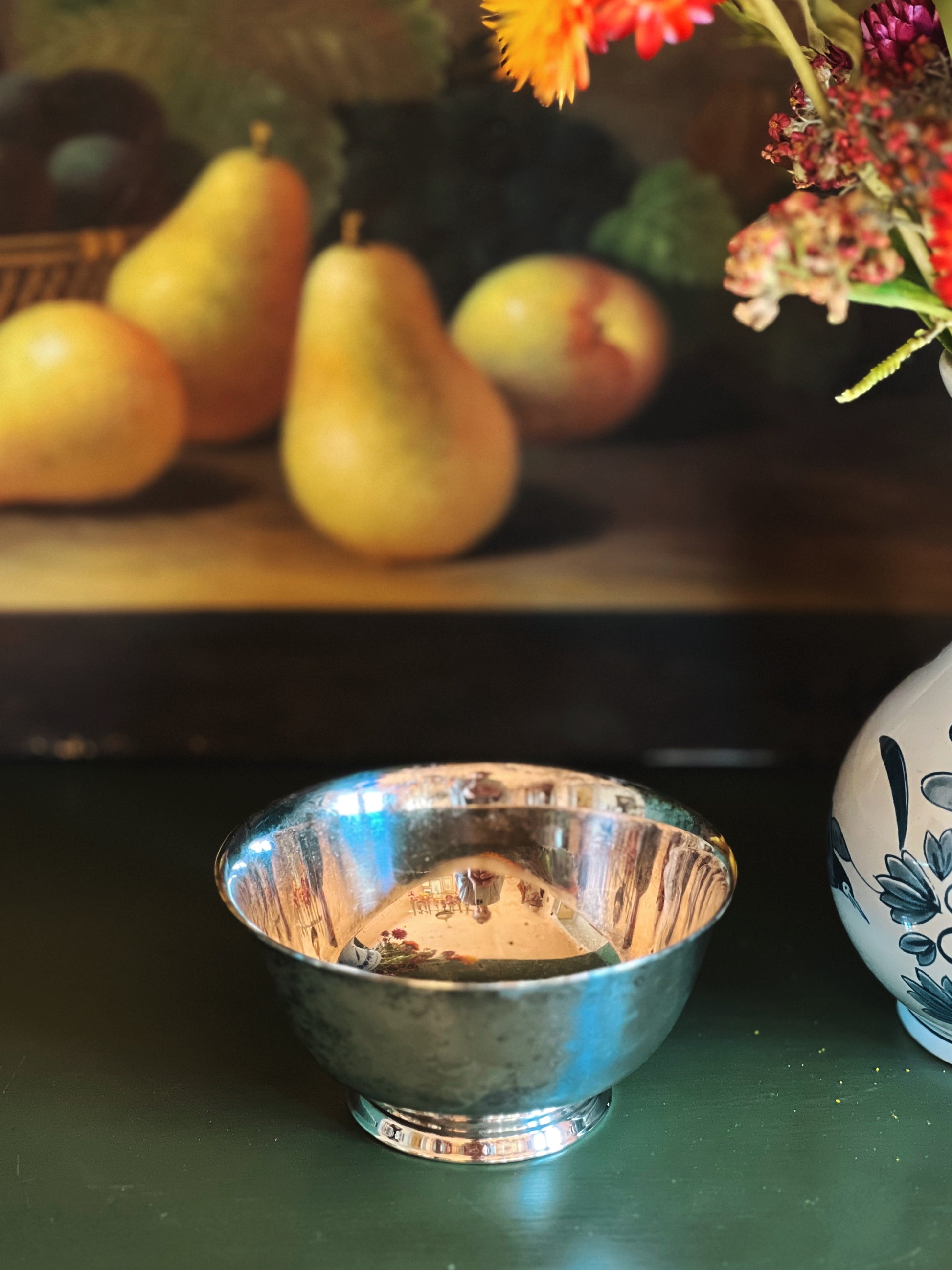 Silver bowl on a table with pears and flowers in the background
