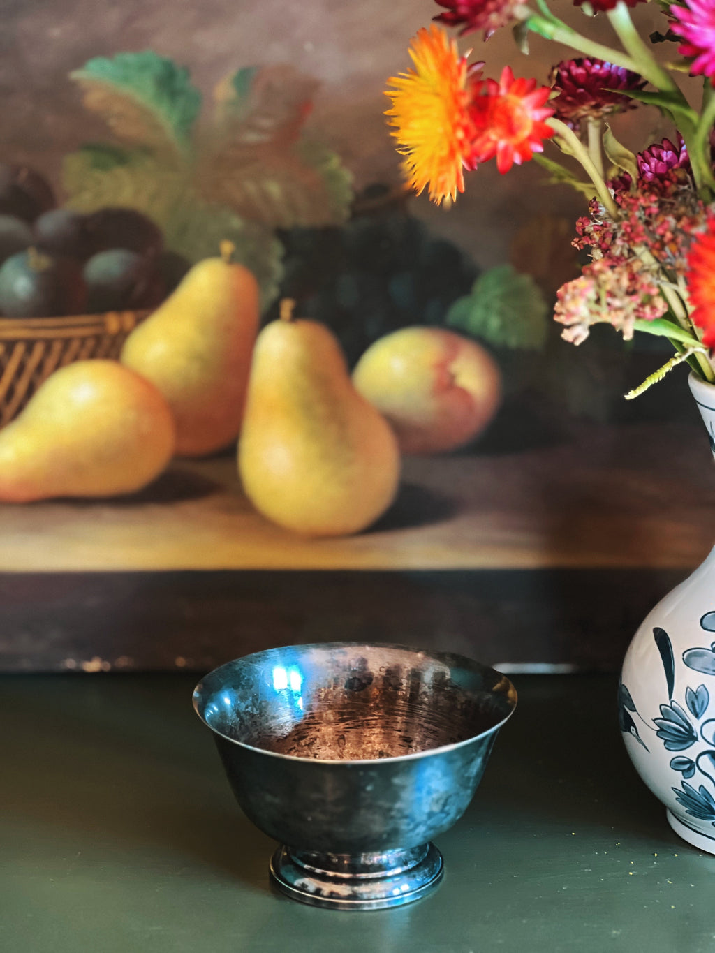 Silver bowl on a table with pears, peaches, and flowers in the background