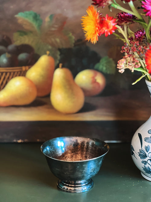 Silver bowl on a table with pears, peaches, and flowers in the background