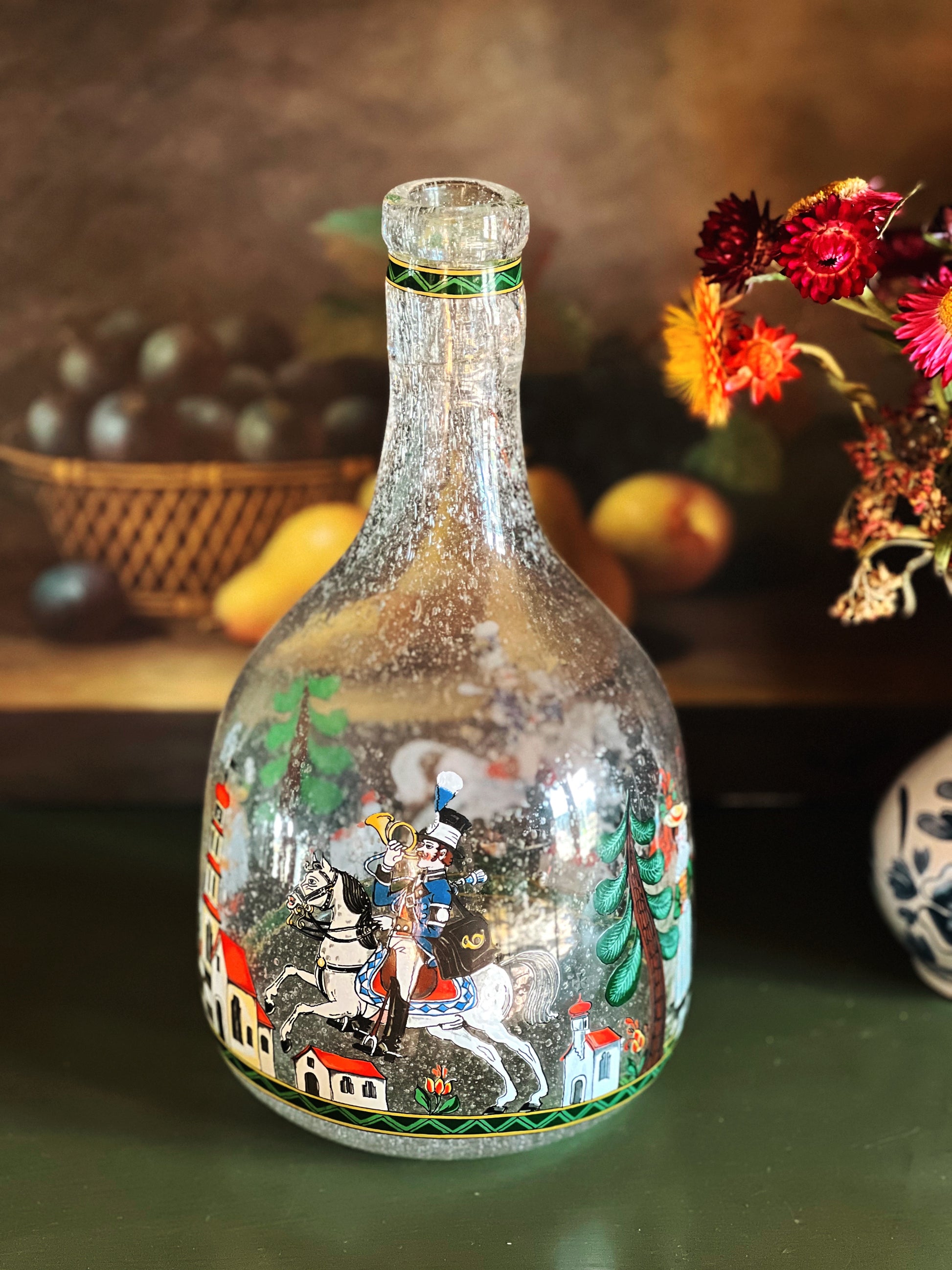 Decorative glass bottle with artistic design on a wooden surface with fruits and flowers in the background