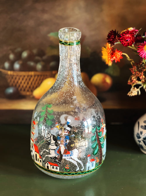 Decorative glass bottle with artistic design on a wooden surface with fruits and flowers in the background