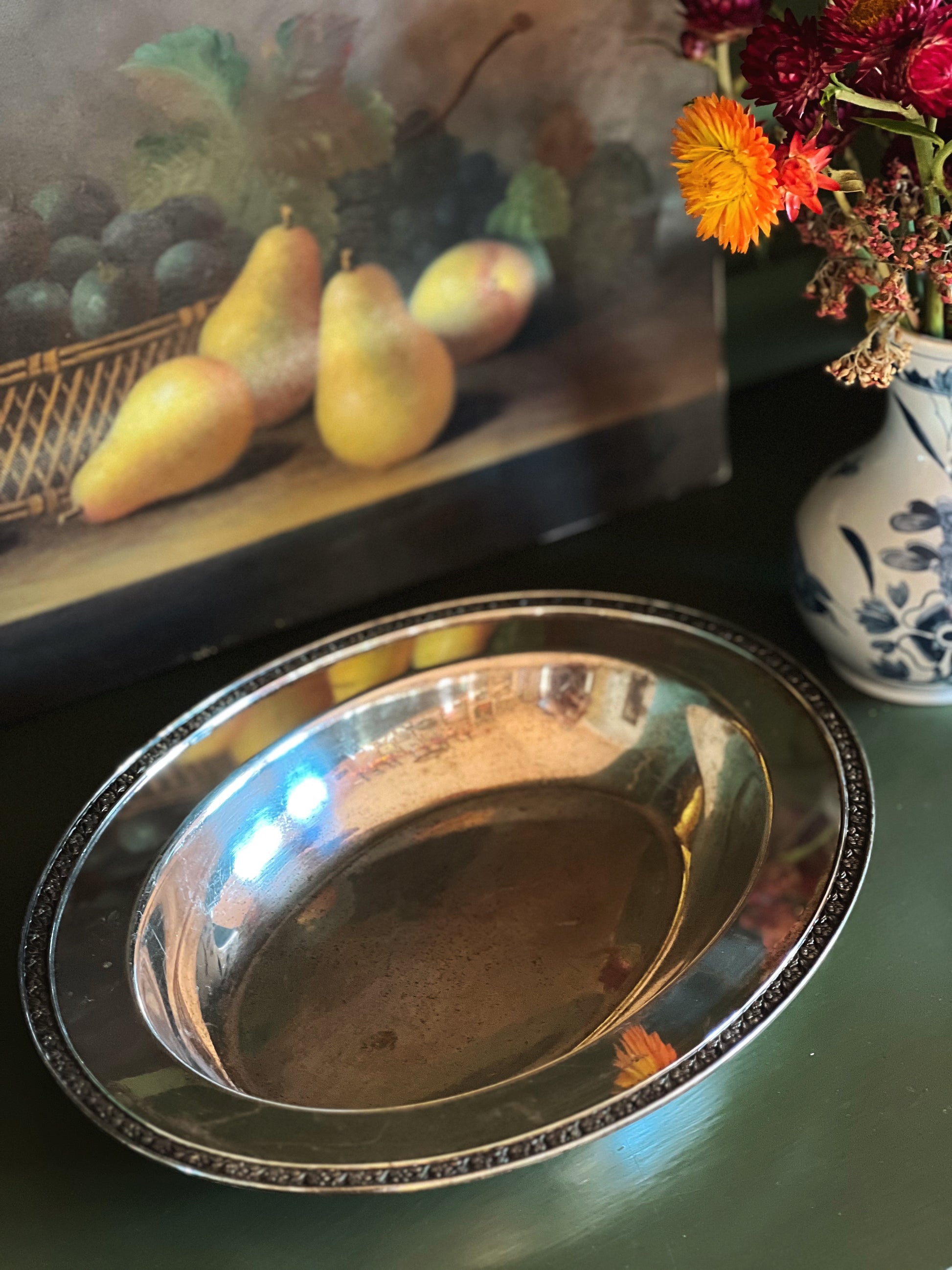 Silver platter on a table with a painting and flowers in the background