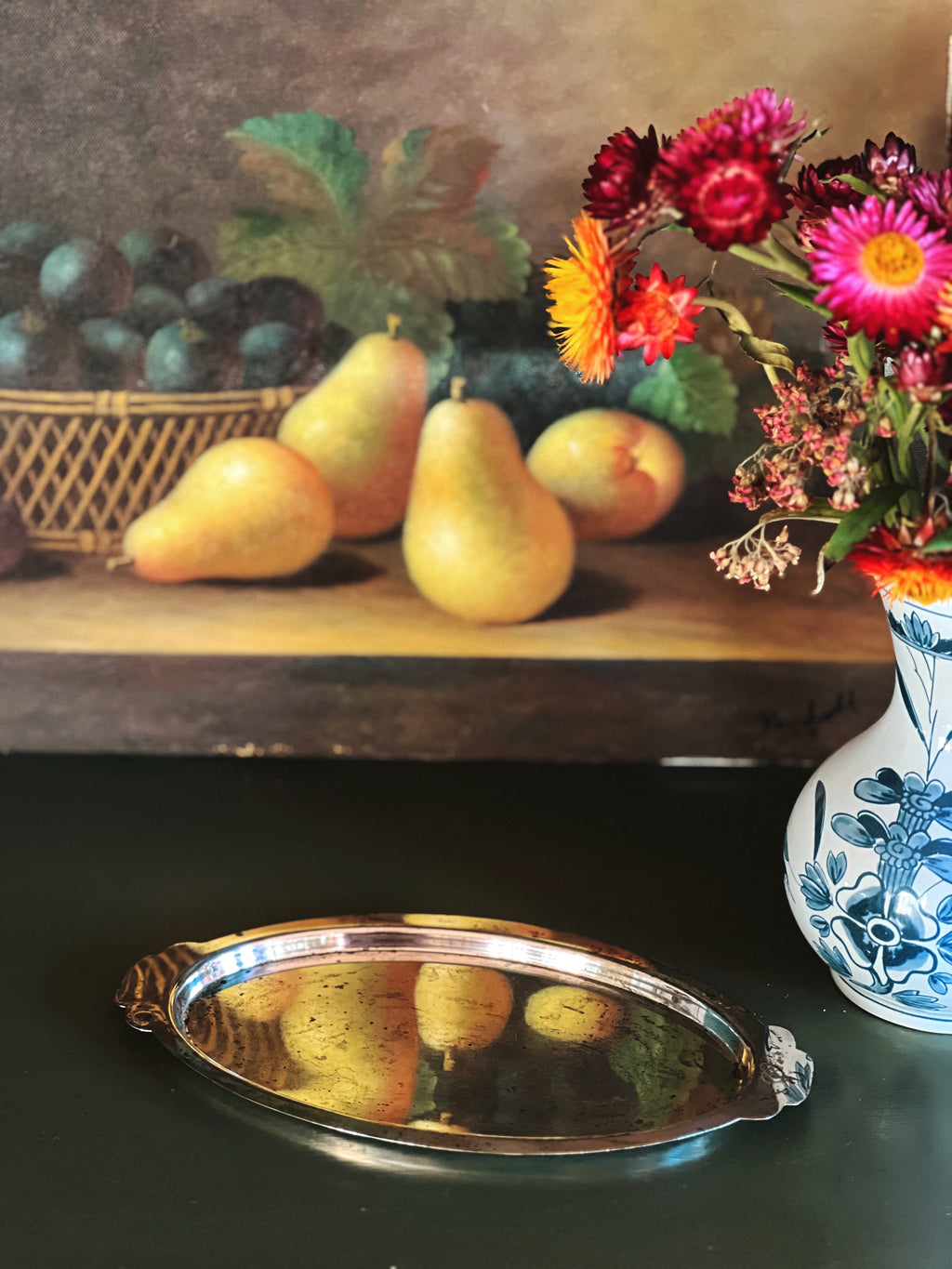 Still life arrangement with pears, grapes, and flowers on a wooden shelf.