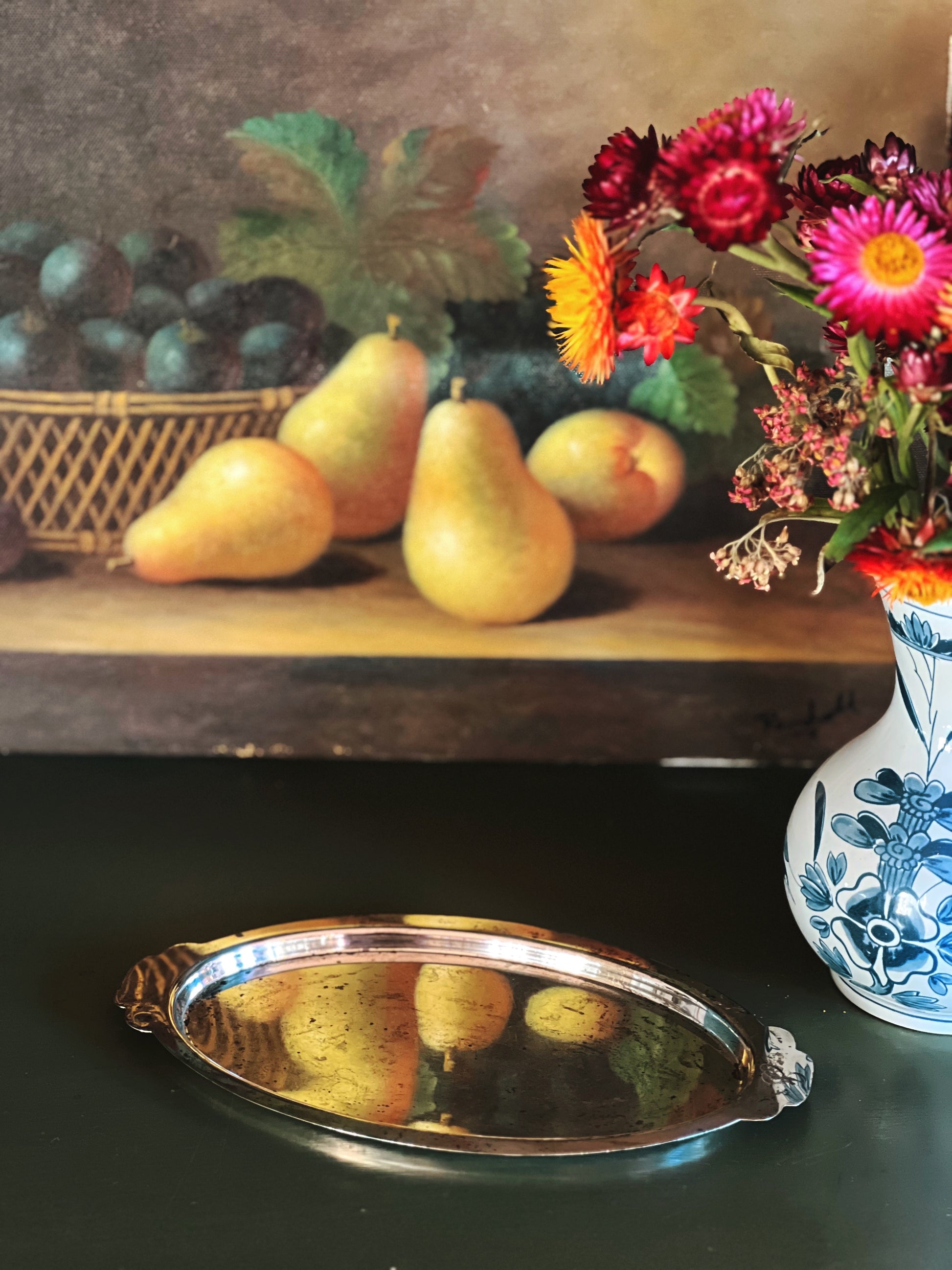 Still life arrangement with pears, grapes, and flowers on a wooden shelf.