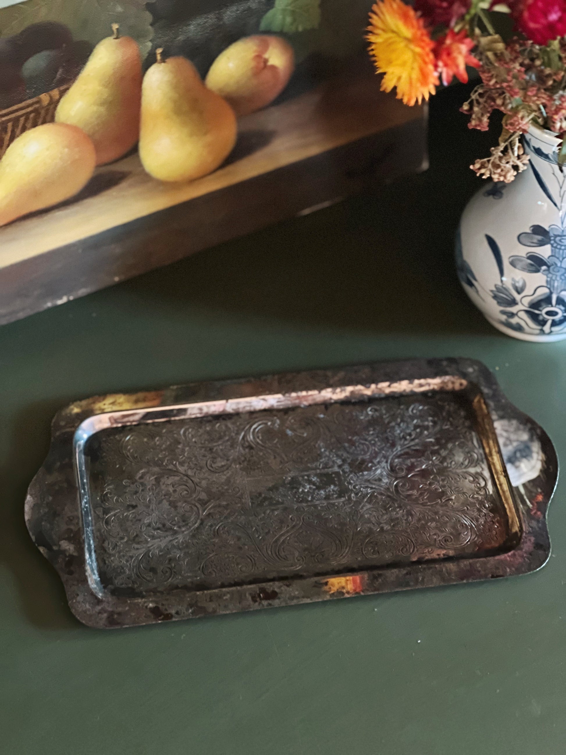 Rustic metal tray on a green surface with pears and flowers in the background