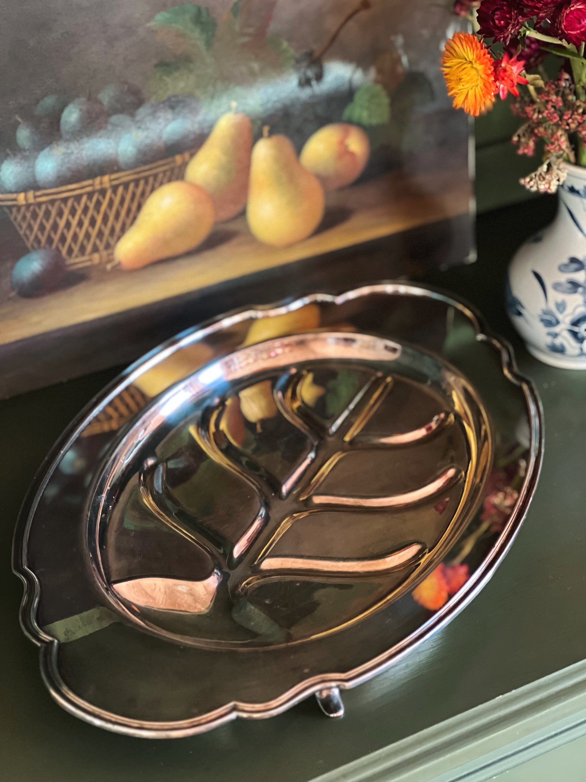 Decorative silver dish with a fruit painting in the background