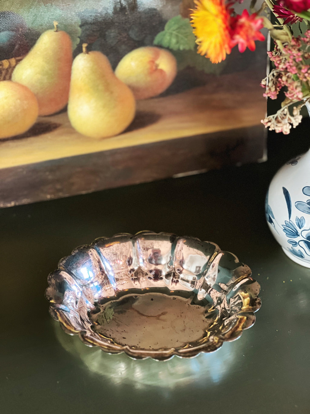 Decorative silver dish on a dark surface with pears and flowers in the background
