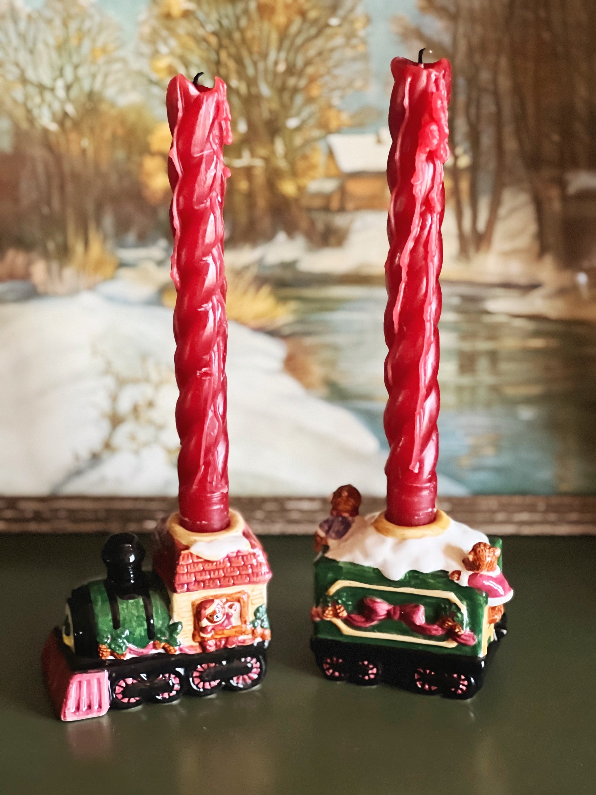 Red twisted candles on decorative train stands with a winter scene in the background