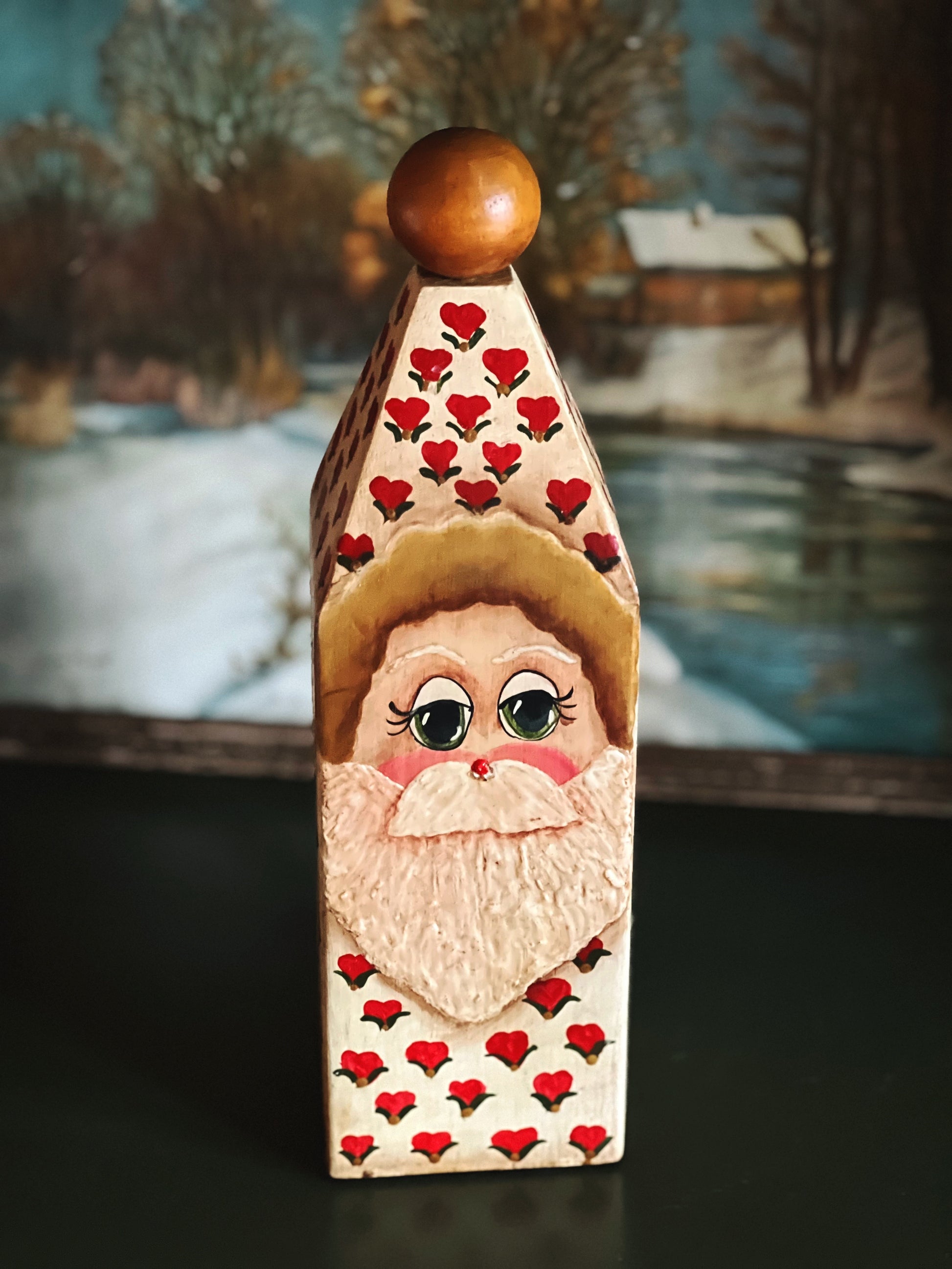 Wooden decorative piece with a face and red hearts, set against a winter landscape.