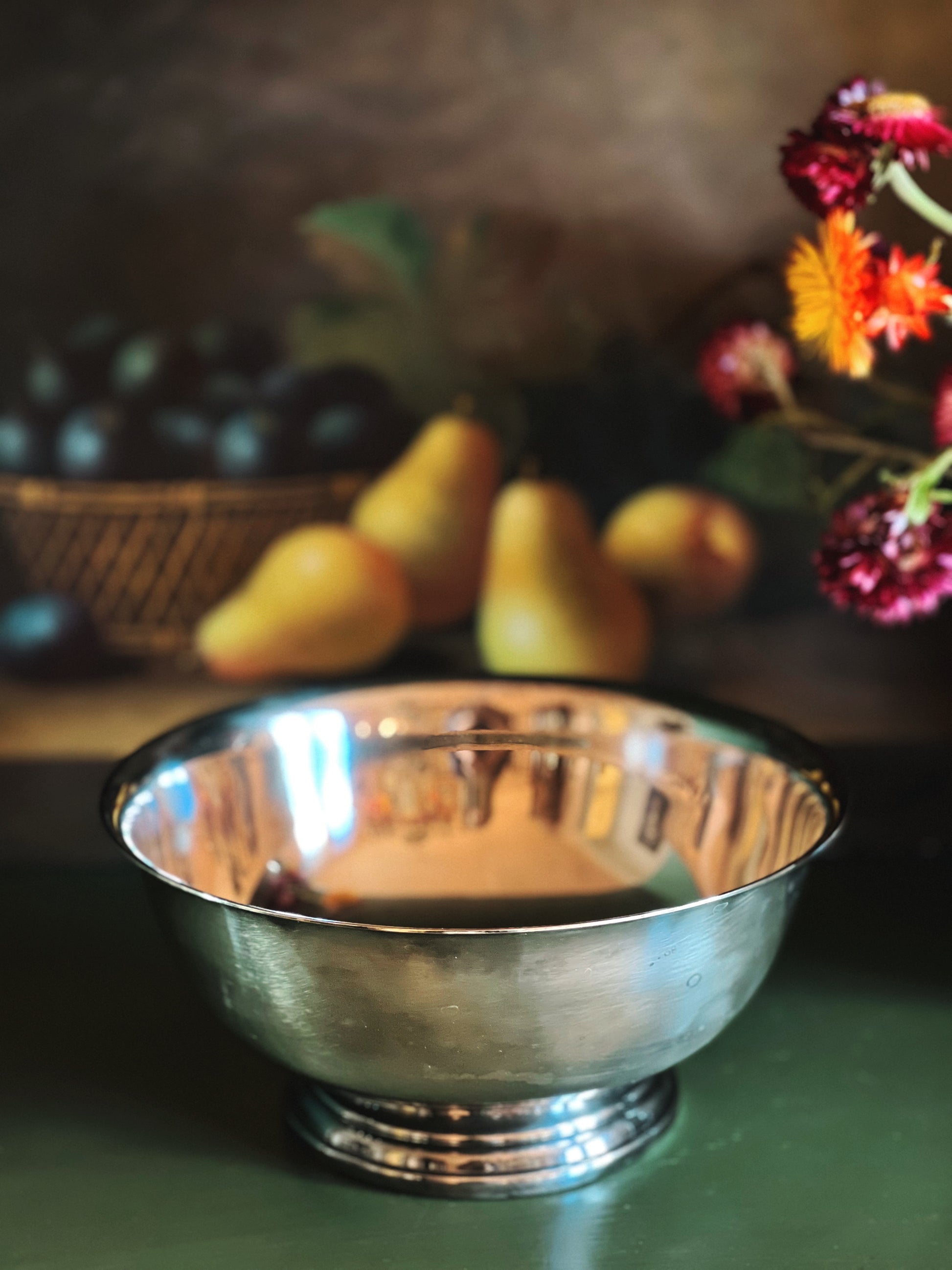 Silver bowl on a table with pears and flowers in the background