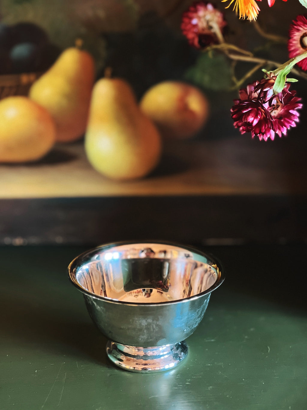 Silver bowl on a dark surface with pears and flowers in the background