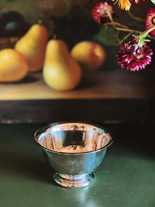 Silver bowl on a dark surface with pears and flowers in the background