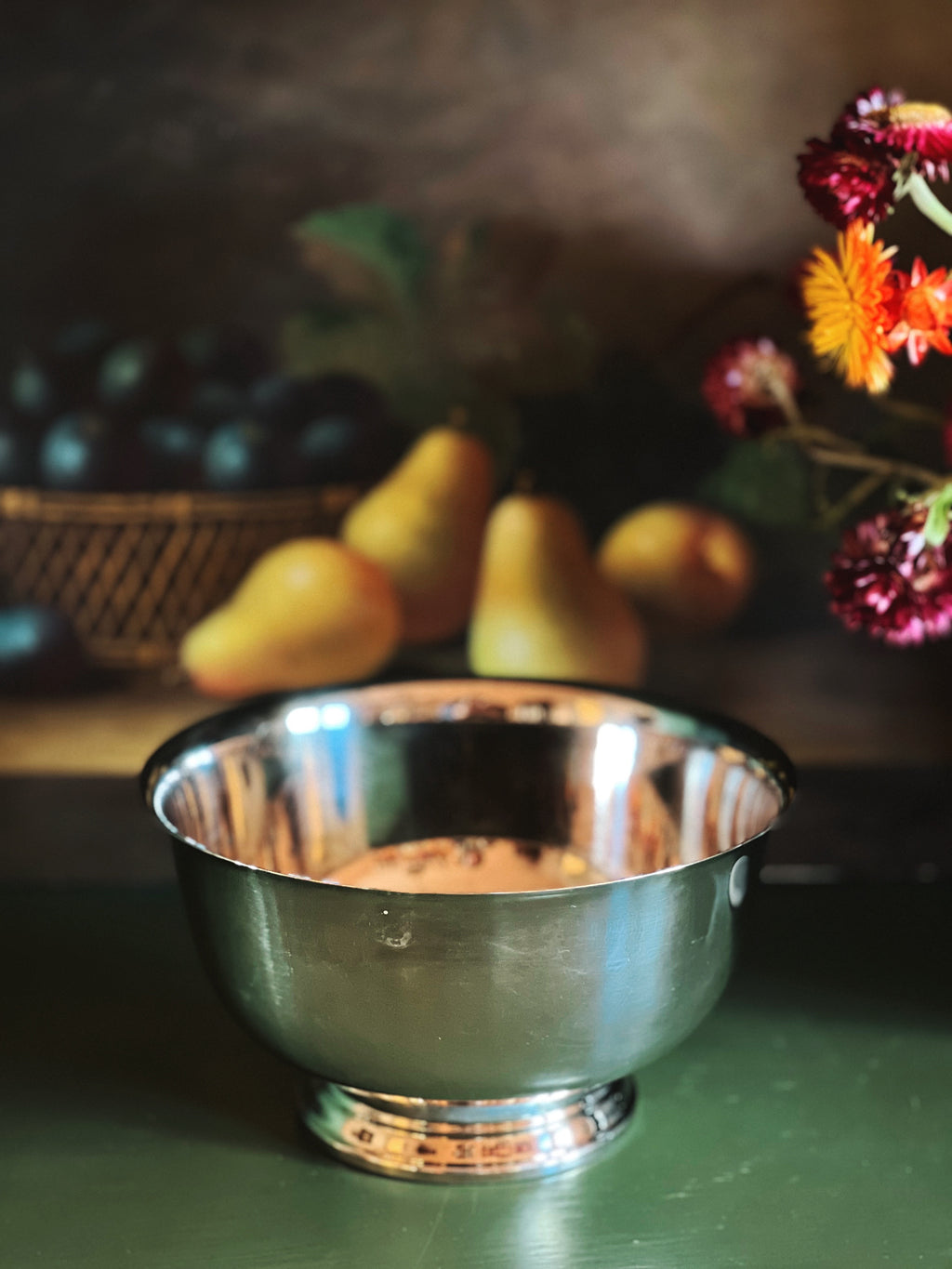 Silver bowl on a table with pears and flowers in the background