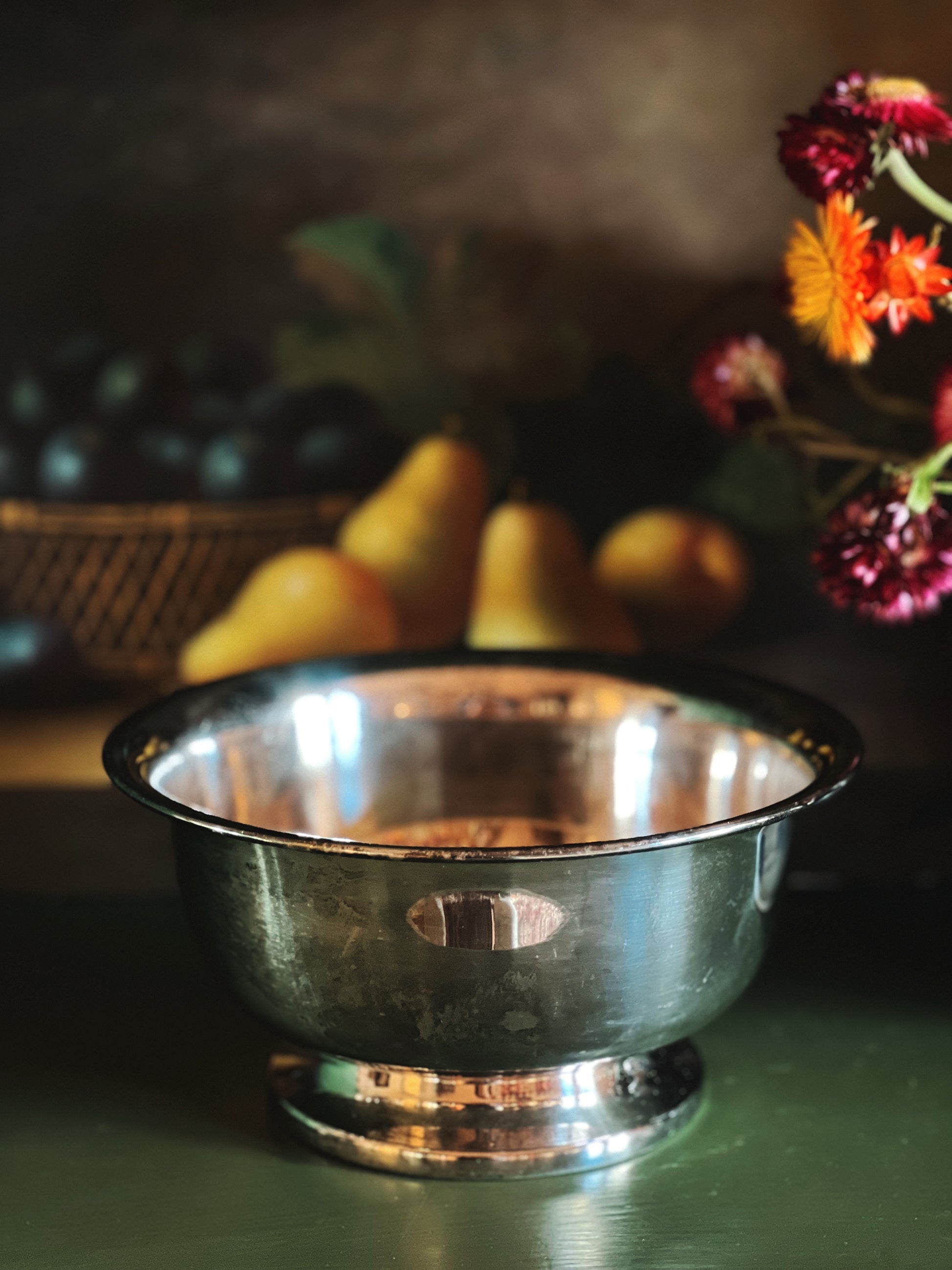 Silver bowl on a table with pears and flowers in the background