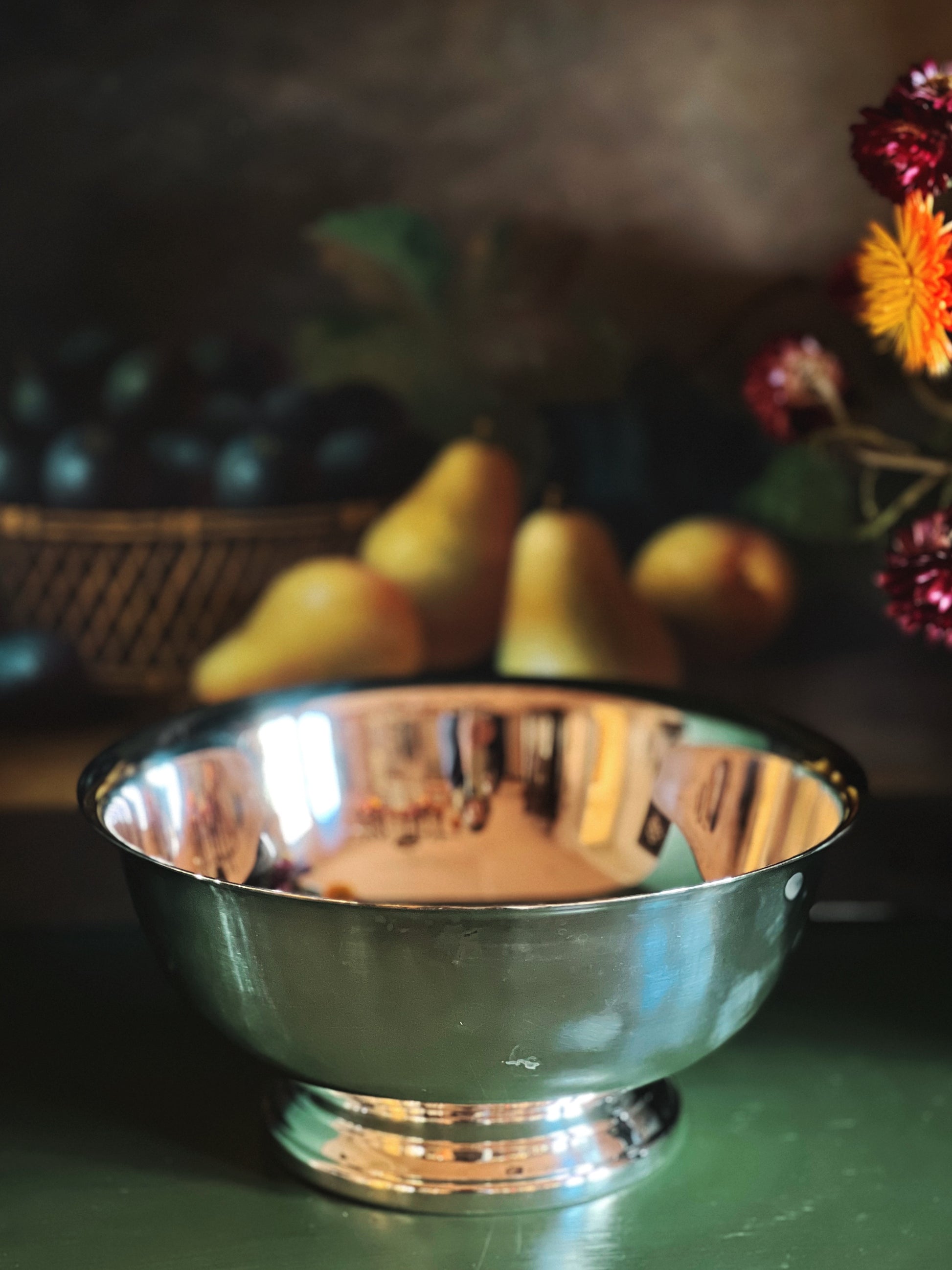 Silver bowl on a table with pears and flowers in the background