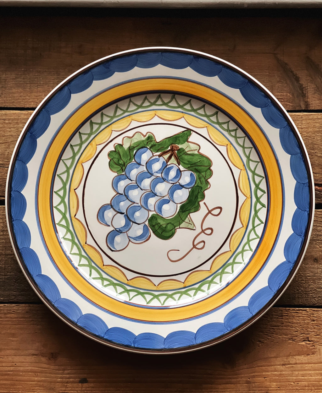 Decorative ceramic plate with grape design on a wooden surface