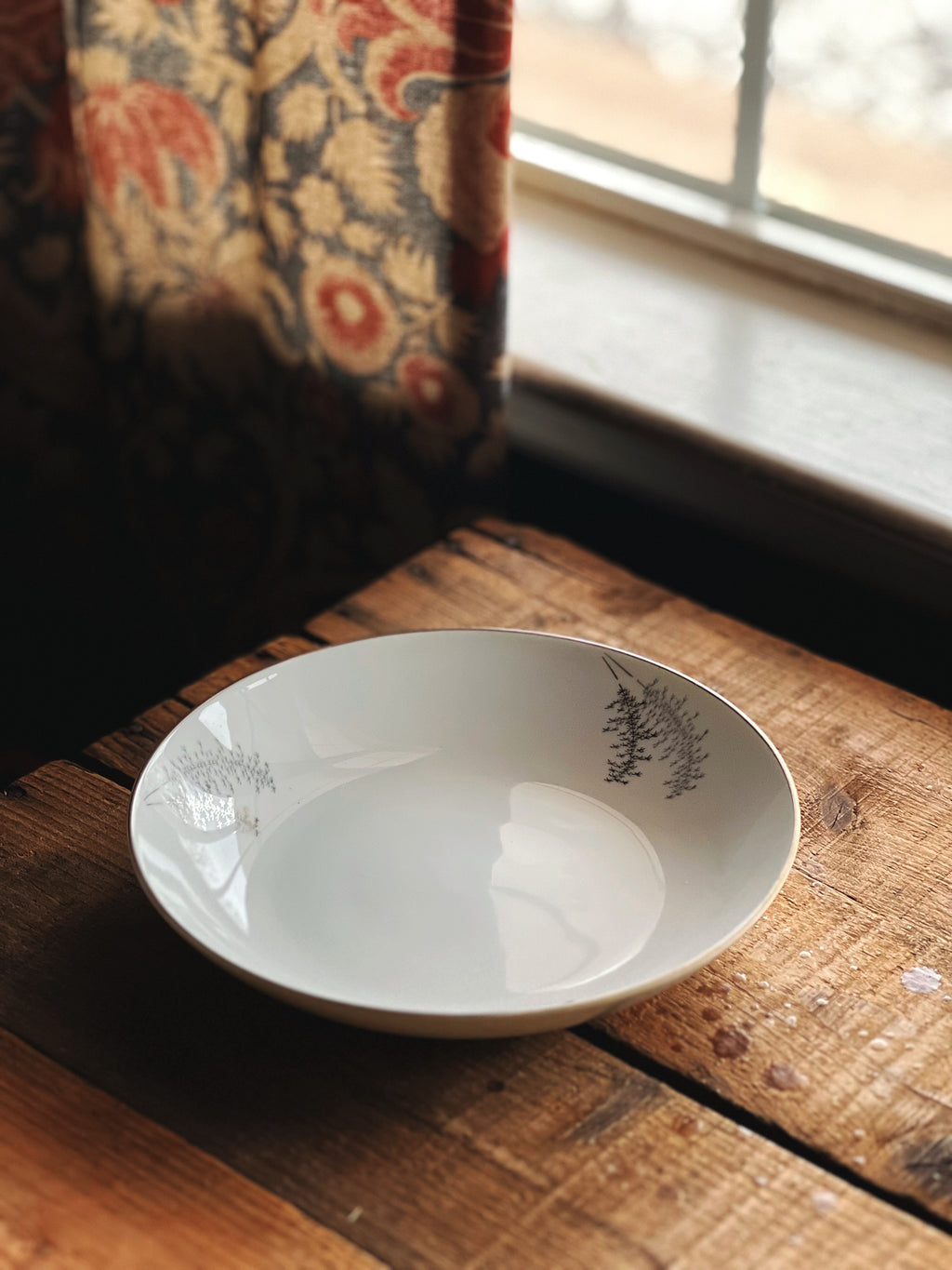 White ceramic bowl with floral design on a wooden surface near a window