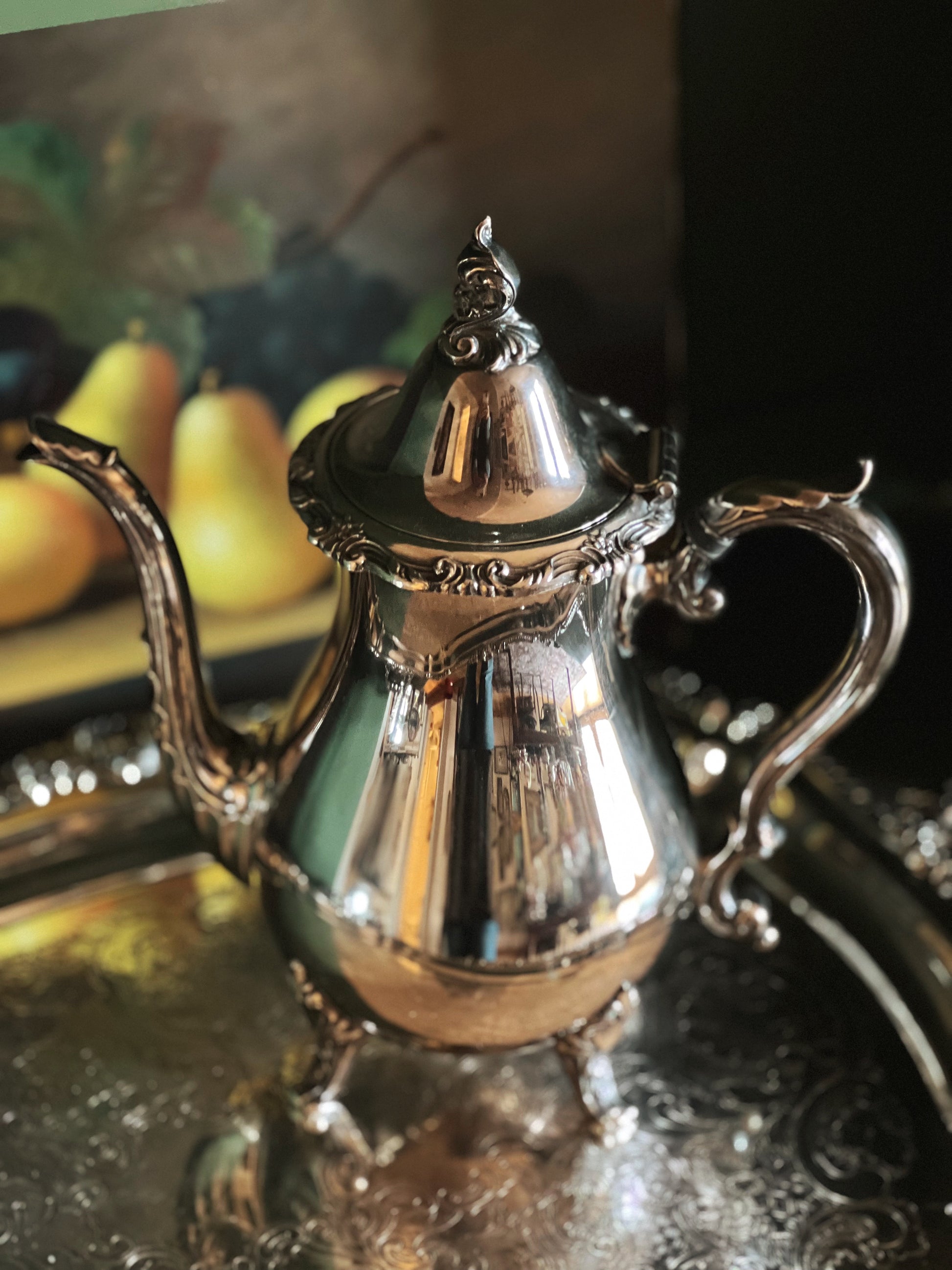Silver teapot on a reflective surface with a blurred background