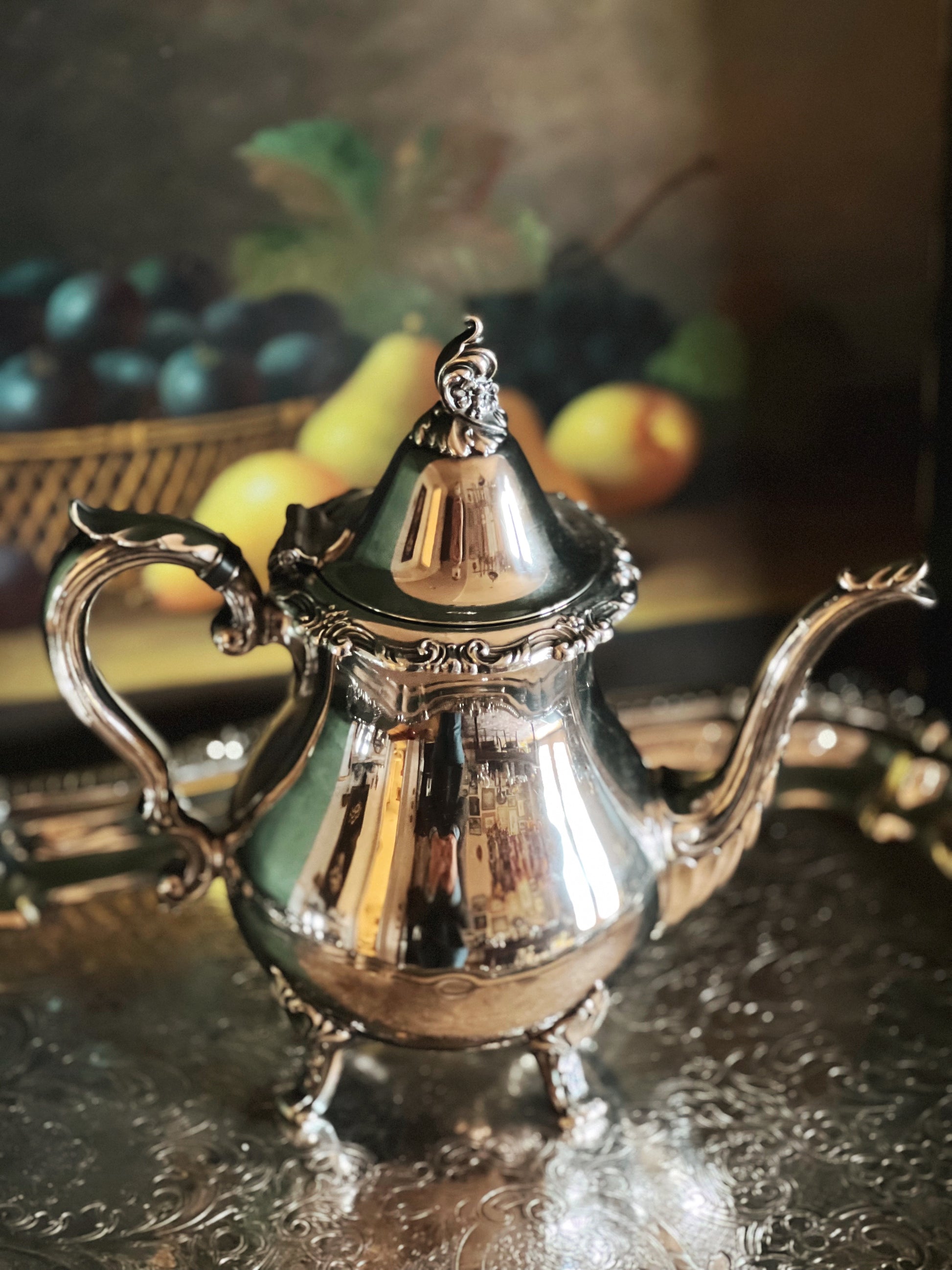 Silver teapot on a reflective surface with a blurred background