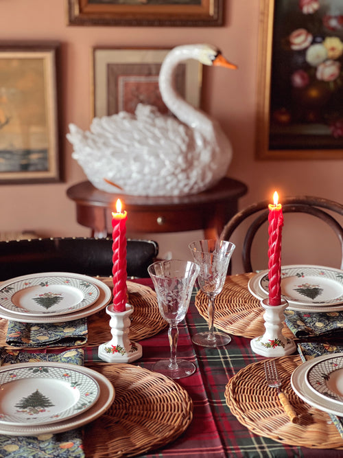Decorative table setting with red candles, wicker placemats, and a swan sculpture in the background.