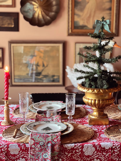 Decorative Christmas table setting with a small tree, candles, and patterned tablecloth.