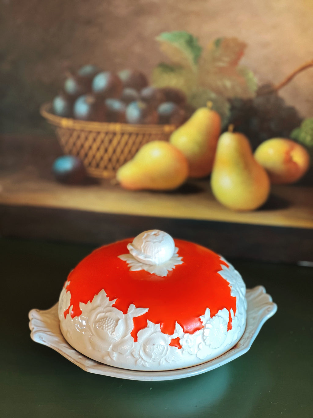 Decorative cake with red and white icing on a table with fruit in the background