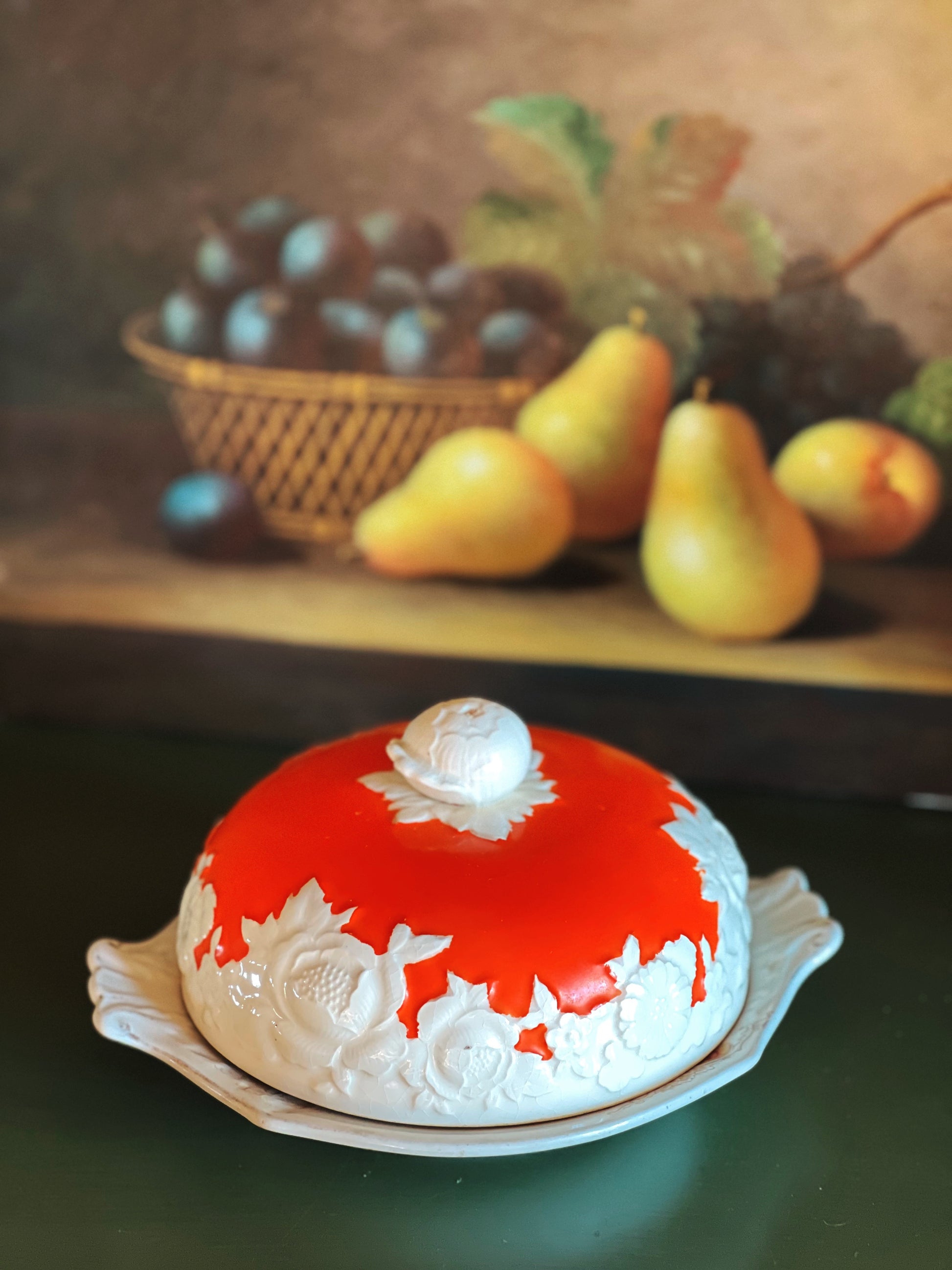Decorative cake with red and white icing on a table with fruit in the background