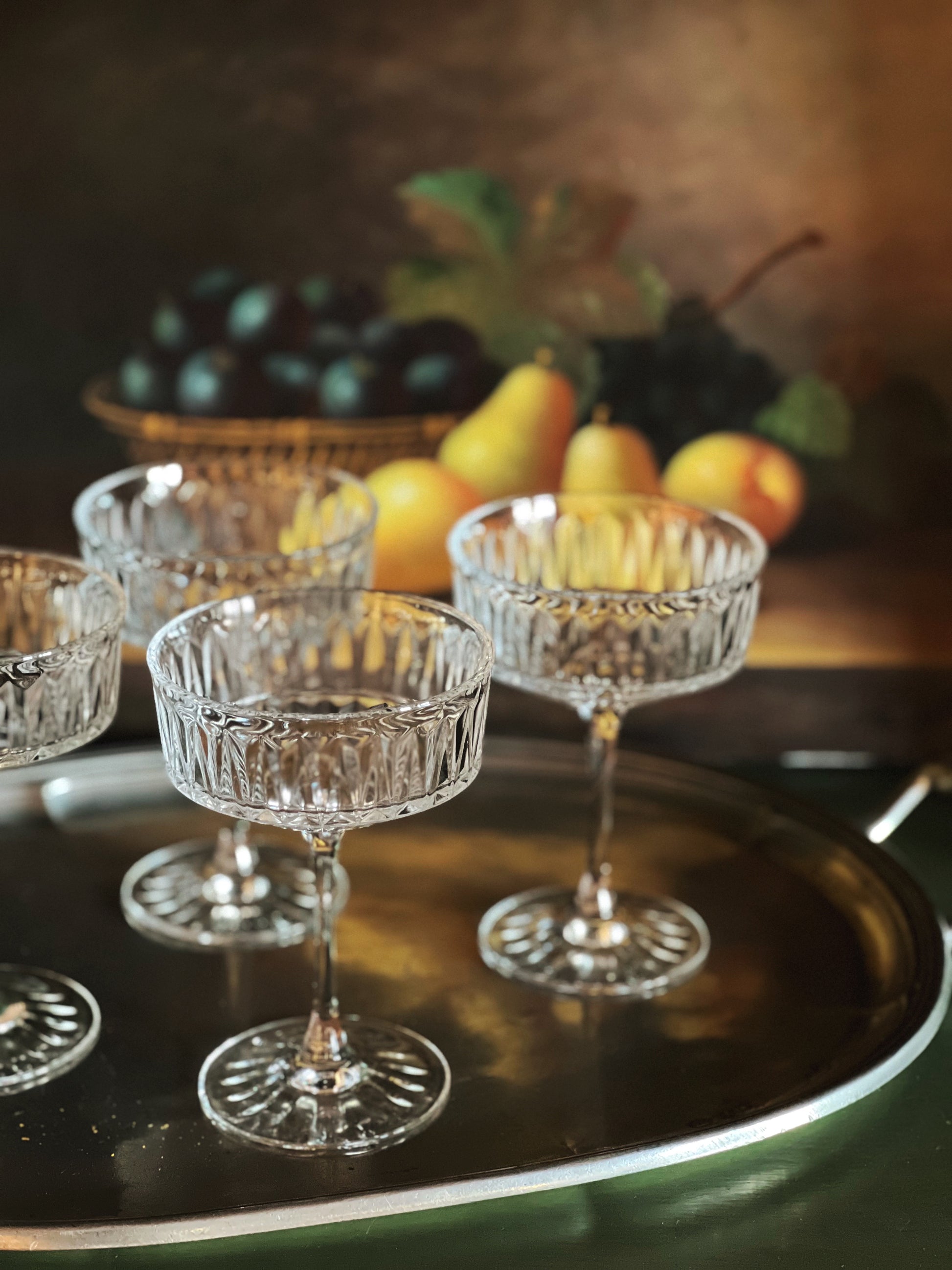 Set of crystal glasses on a tray with fruits in the background