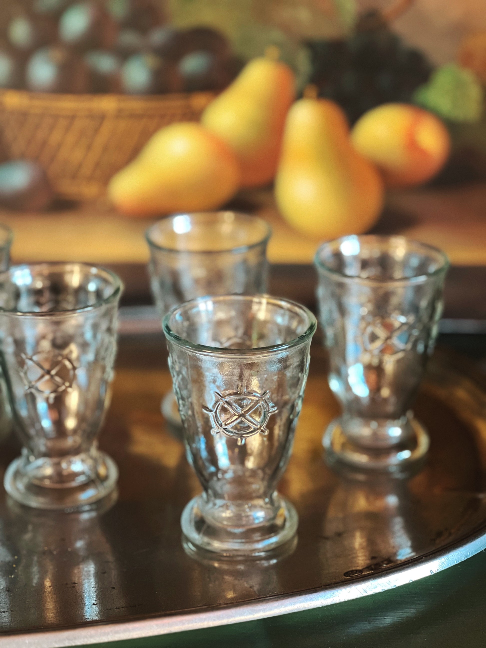 Clear glass tumblers with intricate designs on a wooden surface with pears in the background