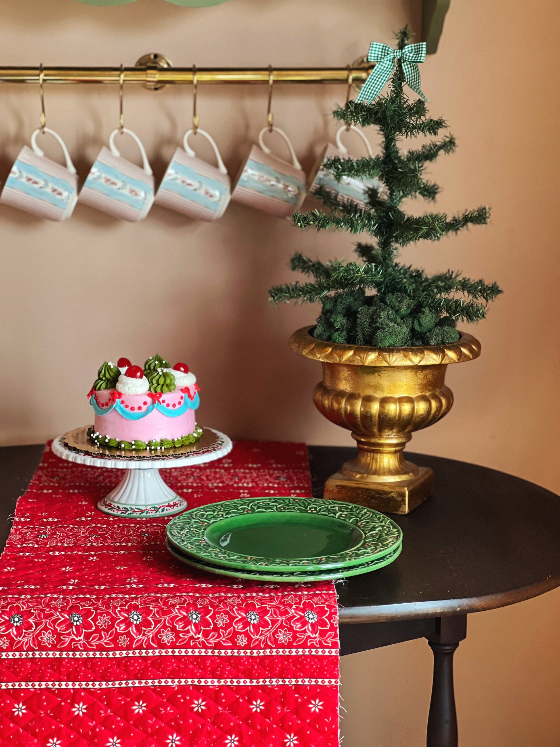 Decorative table setting with a small Christmas tree, cake, and mugs on a red tablecloth.