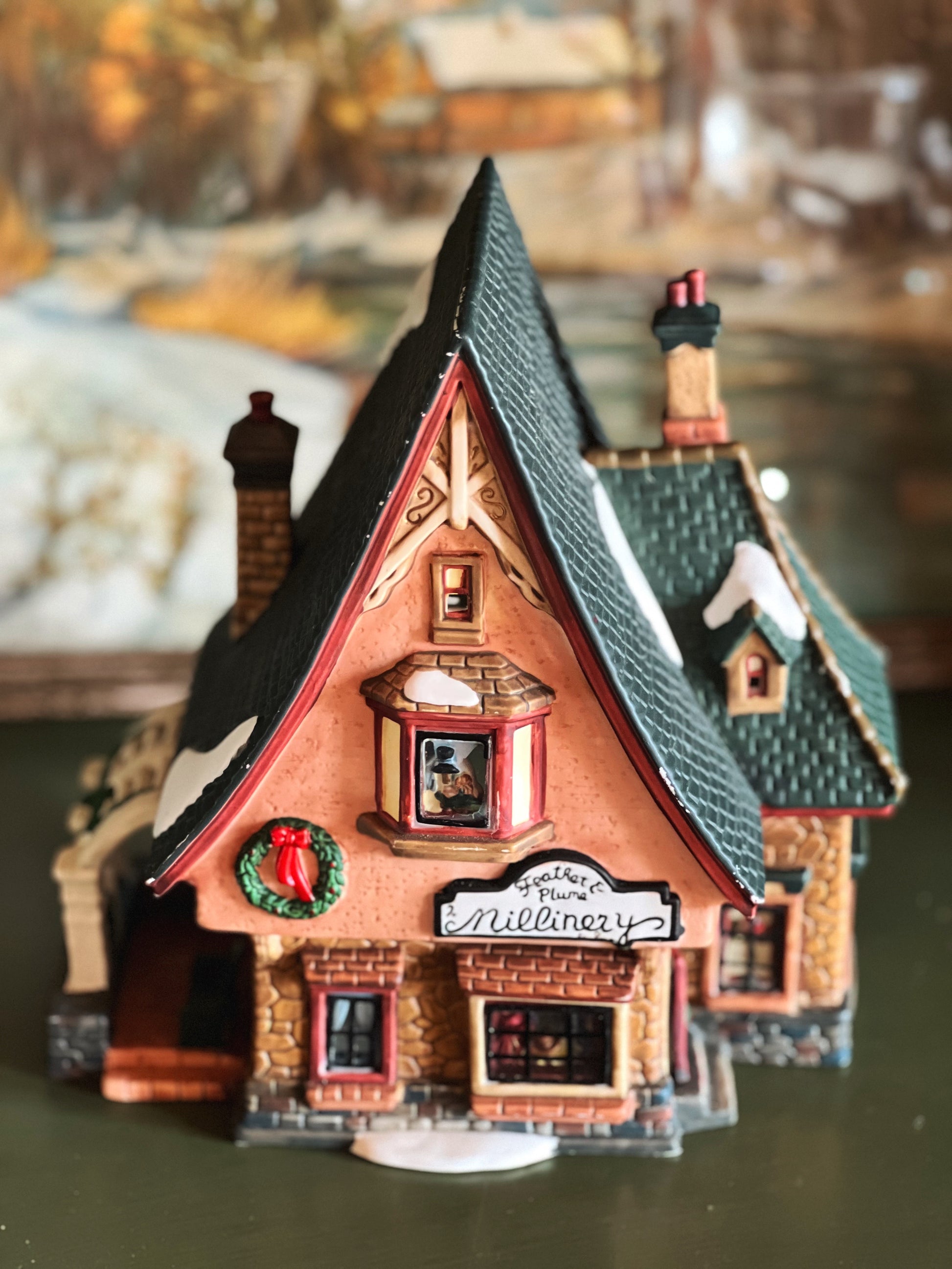Decorative model of a quaint house with a sign reading 'Mills' Millinery' on a blurred background.