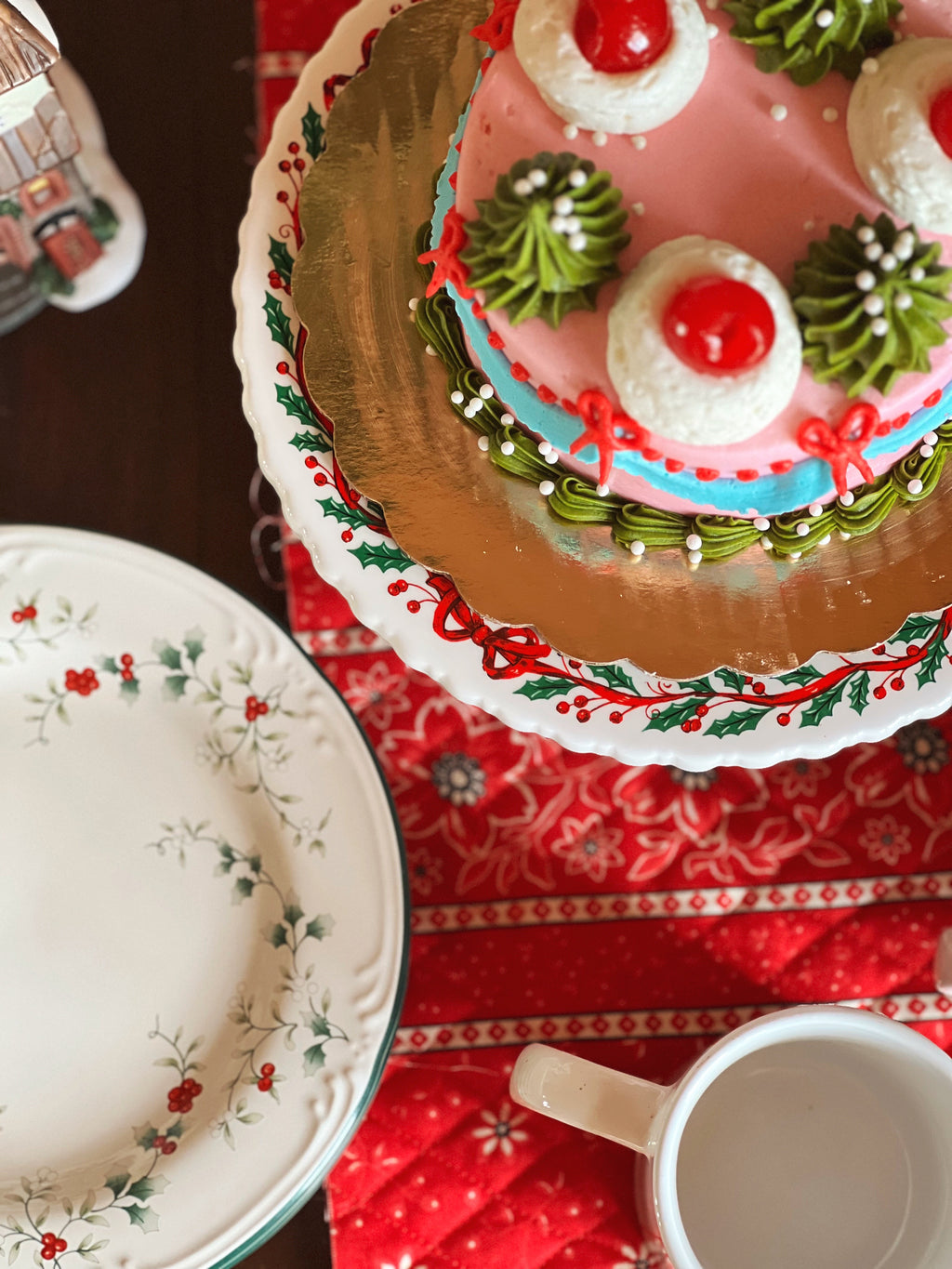 Decorative Christmas cake on a stand with a red and white patterned tablecloth.