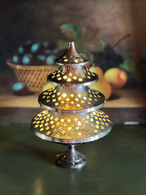 Decorative metal lantern with cut-out patterns on a reflective surface.