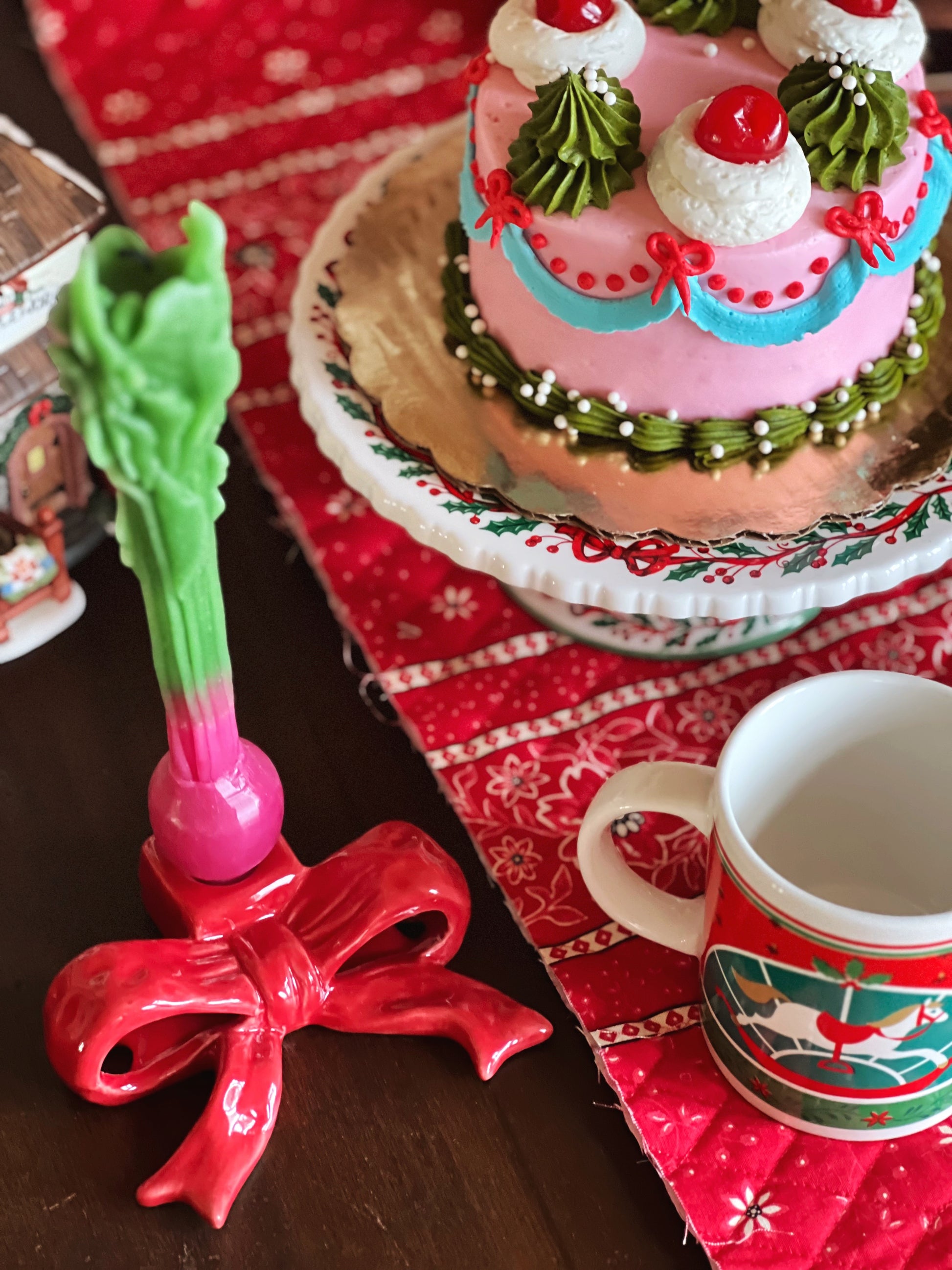 Decorative cake with green and red accents on a table with a mug and decorative item.