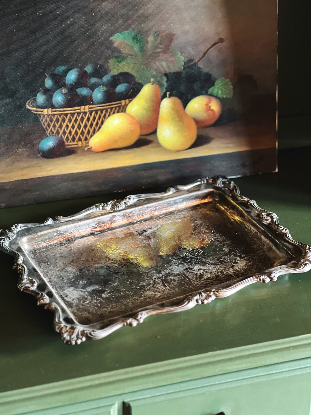 Decorative silver tray in front of a painting of fruit