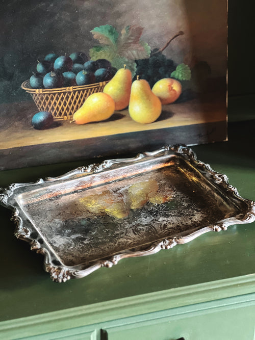 Decorative silver tray in front of a painting of fruit