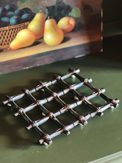 Decorative metal trivet on a green surface with a painting of pears in the background.