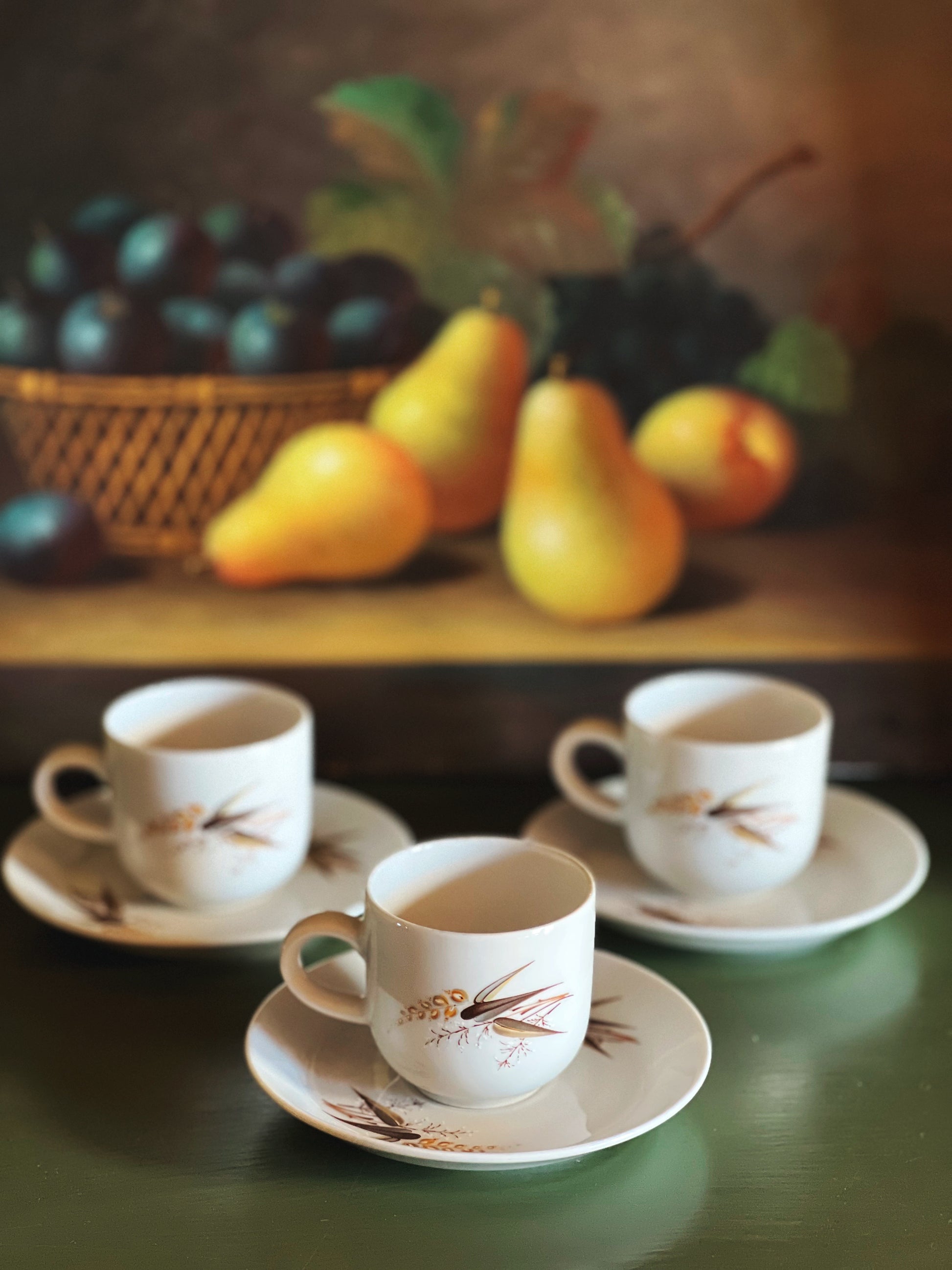 Three white cups with decorative handles on saucers, set against a rustic background with pears and plums.