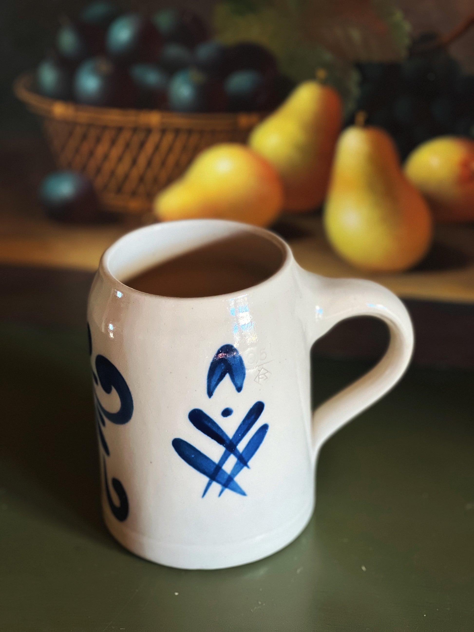 White mug with blue designs on a table with fruits in the background