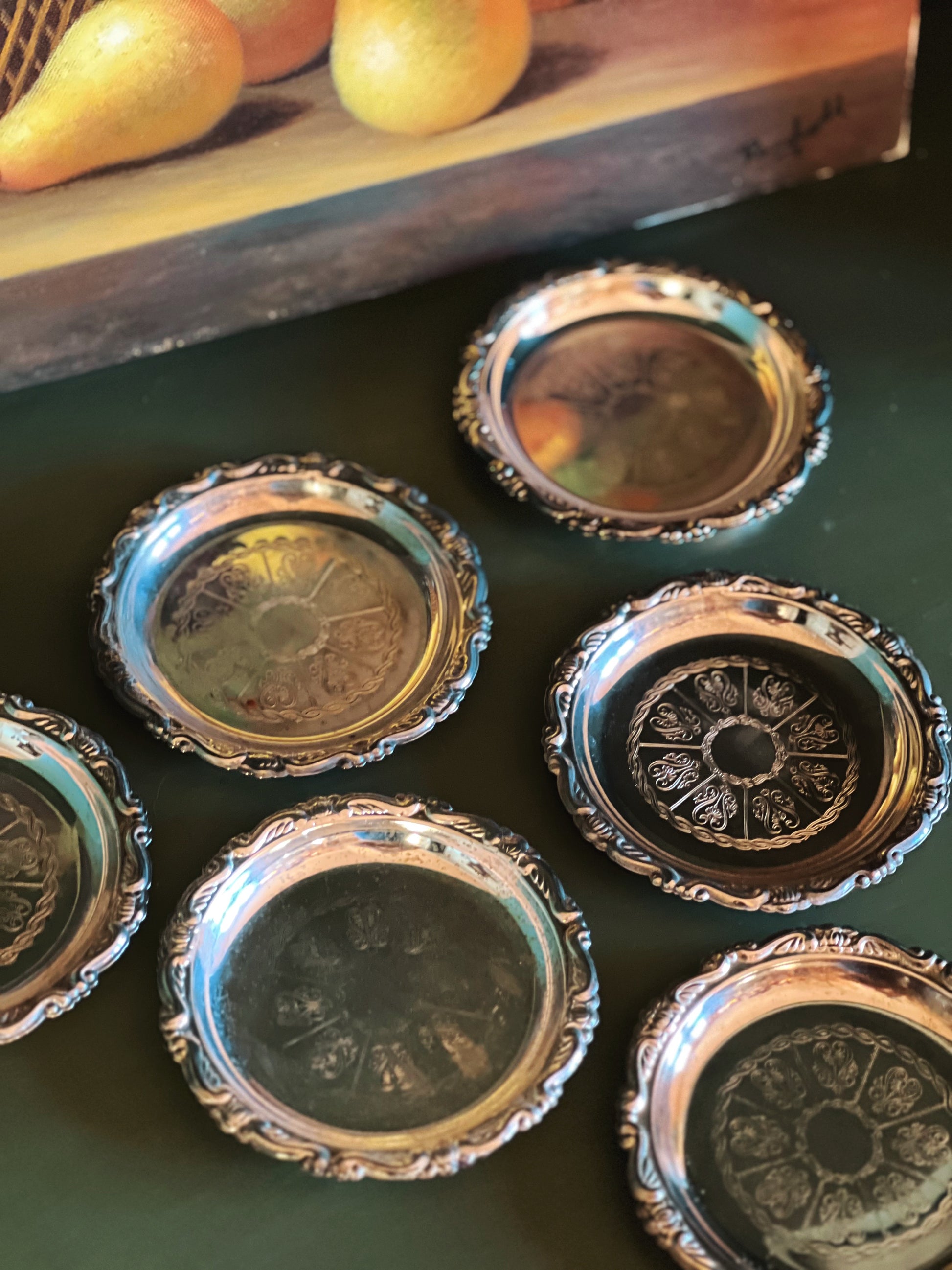 Set of decorative silver coasters on a dark surface with fruits in the background